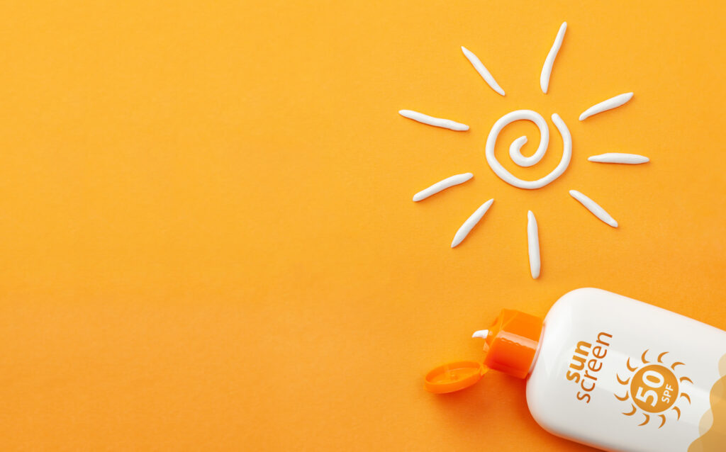 Sunscreen on orange background. Plastic bottle of sun protection and white sun-shaped cream.